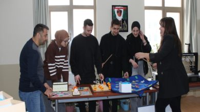 Bir sınıfta veya atölyede, bir grup öğrenci ve bir öğretim üyesi masa üzerindeki materyalleri inceliyor. Masada görme engelli bireylerin eğitimi için tasarlanmış dokunsal oyunlar ve renkli eğitim materyalleri bulunuyor. Katılımcıların materyallere odaklandığı bu kare, özel eğitim alanındaki uygulamalı çalışmaları yansıtıyor.