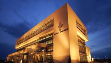 Fotoğrafta gece saatlerinde ışıklandırılmış modern bir kamu binası görülüyor. Binanın cephesinde Anayasa Mahkemesi yazısı ve amblemi yer alıyor. Geniş cam cepheli ve çok katlı yapı, resmi ve kurumsal mimarisiyle dikkat çekiyor.