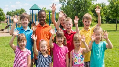 Bir parkta çekilen görüntüde, farklı çocuklar yan yana durup ellerini kaldırarak gülümsüyor. Renkli kıyafetler içindeki grup, neşe, birlik ve kapsayıcılık hissini yansıtıyor.
