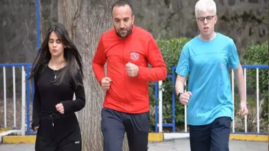 Açık alanda çekilmiş fotoğrafta üç kişi birlikte koşuyor. Ortada kırmızı eşofman üstü giyen bir yetişkin erkek, iki yanında ise spor kıyafetli gençler var. Soldaki siyah eşofmanlı genç kadın, sağdaki ise mavi tişörtlü genç erkek. Park benzeri bir ortamda, ağaç ve korkulukların bulunduğu bir alanda antrenman yaparken görüntülenmişler.