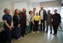 Bir hastane odasında, sağlık çalışanları ve sivil kişilerden oluşan bir grup yan yana durarak fotoğraf veriyor. Ortada ayakta duran yaşlı bir hasta dikkat çekerken, etrafında doktorlar ve sağlık personeli yer alıyor. Ortam, başarılı bir tedavi ya da ameliyat sonrası çekilmiş bir hatıra fotoğrafını andırıyor.