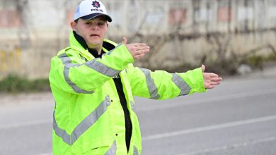 Neon sarı reflektörlü mont ve “polis” yazılı şapka giyen Down sendromlu Fırat Öztürk, yolda araçların yönünü elleriyle işaret ederek trafiği düzenliyor.