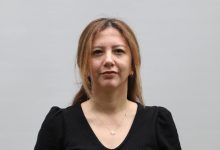 Düz, açık renkli bir arka plan önünde çekilmiş bir portre. Omuz hizasında kadraja alınmış bir kadın doğrudan kameraya bakıyor. Siyah bir bluz giymiş ve ince bir kolye takıyor. Yüz ifadesi sakin ve ciddi; fotoğraf kurumsal ya da haber amaçlı bir çekim izlenimi veriyor.