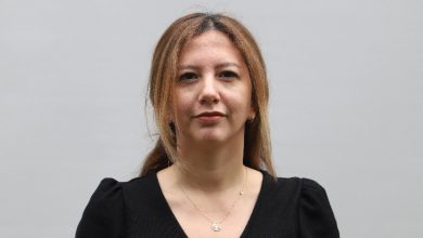 Düz, açık renkli bir arka plan önünde çekilmiş bir portre. Omuz hizasında kadraja alınmış bir kadın doğrudan kameraya bakıyor. Siyah bir bluz giymiş ve ince bir kolye takıyor. Yüz ifadesi sakin ve ciddi; fotoğraf kurumsal ya da haber amaçlı bir çekim izlenimi veriyor.