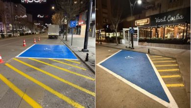 Görselde, gece saatlerinde bir şehir caddesinde engelli bireyler için ayrılmış park alanları görülüyor. Mavi zemin üzerine tekerlekli sandalye sembolü çizilmiş ve sarı çizgilerle park sınırları belirlenmiş. Yol kenarında yer alan bu alanlar, engelli sürücülerin araçlarını rahatça park edebilmesi için düzenlenmiş özel park yerlerini gösteriyor. Arkada mağazalar ve sokak aydınlatmaları da dikkat çekiyor.