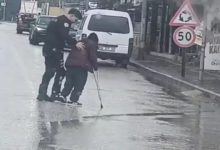 Yağmurlu bir günde çekilen görüntüde, bir polis memuru bastonla yürüyen engelli bir bireyin koluna destek olarak onu yolun karşısına geçirmeye yardımcı oluyor. Islak yolda trafik akışı görülürken, polis memurunun dikkatli şekilde eşlik ettiği an objektife yansımış.