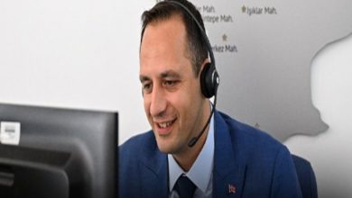 Ofis ortamında, takım elbiseli bir adam kulaklıkla bilgisayar ekranına bakarak gülümsüyor. Bir çağrı merkezi ya da destek hattında çalıştığı izlenimi veriyor; arka planda ise harita benzeri bir pano bulunuyor.