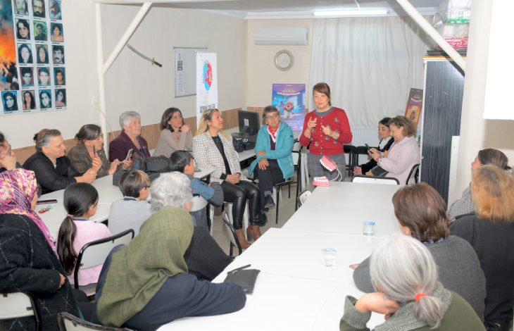 Diş Hekimi Nurhan Çelik Demir, masalarda oturan vatandaşlara ayakta durarak konuşma yapıyor.