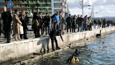 İzmir Kordon boyunda bir denizden çıkarma operasyonunu yansıtıyor. Bir dalgıç denizin içindeyken, rıhtım kenarında bir görevli ona doğru eğilmiş durumda. Kordon boyunca çok sayıda vatandaş ve polis memuru çalışmaları endişeli bir şekilde takip ediyor. Arka planda şehir yapıları ve deniz yüzeyi görülüyor; karede trajik bir olay sonrası yürütülen kurtarma/tespit çalışması betimleniyor.