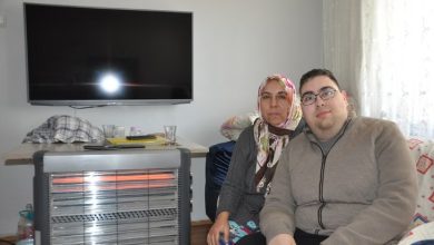 Fotoğrafta bir ev ortamında yan yana oturan bir anne ve oğlu görülüyor. Arkalarında duvara monte edilmiş bir televizyon ve önlerinde elektrikli ısıtıcı bulunuyor. İkili kameraya bakarak birlikte poz veriyor.