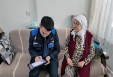 MUSKİ Genel Müdürlüğü personeli erkek yaşlı kadının yanında koltukta oturarak elinde tuttuğu cihazla işlem yapıyor.