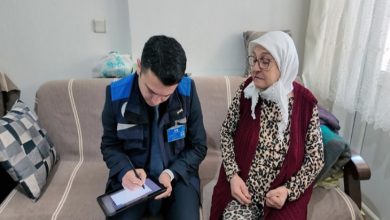 MUSKİ Genel Müdürlüğü personeli erkek yaşlı kadının yanında koltukta oturarak elinde tuttuğu cihazla işlem yapıyor.