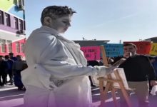 Okul bahçesinde düzenlenen farkındalık etkinliğinde, tamamen beyaza boyanmış bir öğrenci heykel performansı sergiliyor ve tuval üzerine resim yapıyor. Etrafında toplanan öğrenciler etkinliği izlerken, arka planda mesaj içeren pankartlar dikkat çekiyor. Atmosfer, bağımlılık ve farkındalık temalı bir sosyal sorumluluk çalışmasını yansıtıyor.