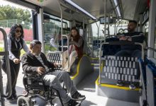 Kadın personel, tekerlekli sandalyedeki erkek yolcuyu otobüsün içine doğru yönlendirirken, içeride diğer özel gereksinimli yolcular koltuklarda oturuyor.