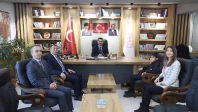 Bir makam odasında çekilen fotoğrafta, İl Millî Eğitim Müdürü masanın arkasında otururken karşısında iki erkek, bir kadın ve bir çocuk koltuklarda oturarak poz veriyor. Odada Türk bayrağı, resmi bayraklar, kitaplıklar ve duvarda Mustafa Kemal Atatürk ile Recep Tayyip Erdoğan’ın portreleri yer alıyor. Ortadaki sehpalarda su şişeleri bulunuyor ve ziyaret resmi bir görüşme havasında gerçekleşiyor.