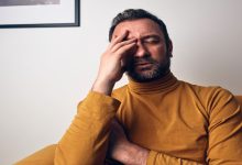 Bir koltukta oturan adam, gözlerini kapatmış şekilde alnını tutuyor. Yüz ifadesi yorgunluk, stres ya da duygusal bir sıkıntıya işaret ederken, sahne zihinsel yük ve içsel bir mücadele hissi veriyor.