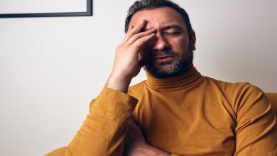 Bir koltukta oturan adam, gözlerini kapatmış şekilde alnını tutuyor. Yüz ifadesi yorgunluk, stres ya da duygusal bir sıkıntıya işaret ederken, sahne zihinsel yük ve içsel bir mücadele hissi veriyor.