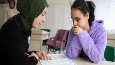 Görme engelli kız öğrenciye, akranı kız öğrenci soru kitapçığı okuyor.