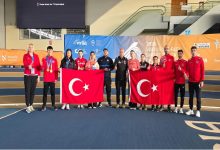 Fotoğrafta kapalı bir spor salonunda toplu halde poz veren sporcular ve antrenörler görülüyor. Sporcuların çoğu kırmızı Türkiye yazılı eşofmanlar giymiş. Grubun ortasında iki kişi büyük Türk bayrakları tutuyor. Bazı sporcuların boynunda kazandıkları madalyalar bulunuyor. Arka planda “2026 Virtus World Short Track Championship” yazılı bir organizasyon panosu yer alırken, sporcular ve teknik ekip kamera karşısında takım halinde gururla poz veriyor.