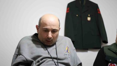 İbrahim Taş, duvarda asılı üniforma önünde oturuyor.