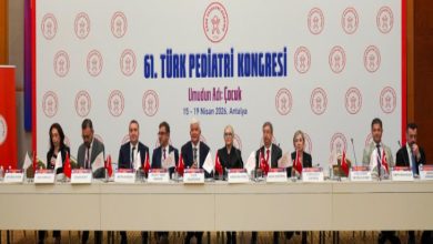 Görselde, 61. Türk Pediatri Kongresi için hazırlanmış bir salonda uzun bir masada yan yana oturan konuşmacılar görülüyor. Masanın üzerinde Türkiye ve kurum bayrakları, isimlikler ve mikrofonlar bulunuyor. Arka planda kongrenin adı, logosu ve “Umudun Adı: Çocuk – 15-19 Nisan 2026, Antalya” yazılı büyük bir pano yer alıyor. Ortam resmi, akademik ve kongre atmosferini yansıtıyor.