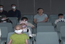 Bir sinema salonunda, çoğu maske takan çocuklar ve yetişkinler koltuklarda oturuyor. Ön sırada saçları dökülmüş, tedavi gördüğü anlaşılan bir çocuk dikkat çekiyor; arka sıralarda ise ona eşlik eden diğer çocuklar ve ebeveynler sakin bir şekilde ekranı izliyor. Atmosfer hem sessiz hem de duygusal bir dayanışma hissi taşıyor.