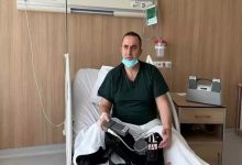 Hastane odasında yatağa oturmuş bir adam görülüyor. Boynunda maskesi var, sakin ama yorgun bir ifadeyle kameraya bakıyor. Kucağında ve yanında kablolarla bağlı taşınabilir bir tıbbi cihaz bulunuyor; bu cihazla yaşamını sürdürüyor gibi görünüyor. Etrafında serum askısı ve tıbbi ekipmanlar yer alıyor.