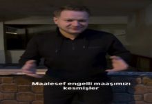 Kapalı bir mekânda ayakta duran bir adam, ellerini kullanarak bir şeyi anlatır gibi konuşuyor. Üzerinde siyah kıyafetler var. Görüntünün alt kısmında “Maalesef engelli maaşımızı kesmişler” yazısı yer alıyor. Sahne, yaşadığı bir mağduriyeti dile getirdiği bir anı yansıtıyor.