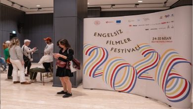 Bir etkinlik alanında, büyük bir pano üzerinde “Engelsiz Filmler Festivali 2026” yazısı yer alıyor. Renkli grafiklerle tasarlanan afişin önünde birkaç kişi ayakta sohbet ediyor ya da telefonlarına bakıyor. Ortam modern ve sakin; festival havası hissediliyor.