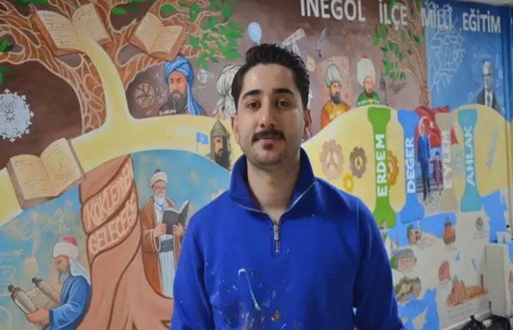 Renkli bir duvar resminin önünde duran bir kişi kameraya doğru bakıyor. Üzerinde boya lekeleri olan mavi bir üst var. Arka planda eğitim temalı figürler, kitaplar ve tarihi karakterlerin yer aldığı detaylı bir mural bulunuyor. Sahne, sanatsal bir çalışmanın ortasında verilen bir röportaj ya da tanıtım anını yansıtıyor.