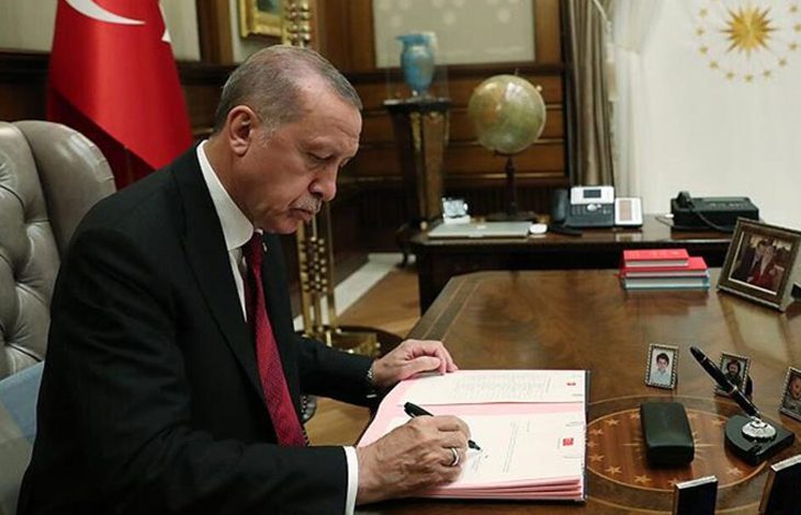 Cumhurbaşkanı Recep Tayyip Erdoğan makamındaki masada oturmuş imza atıyor.