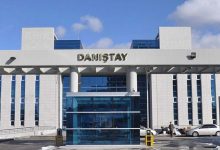 Modern mimariye sahip büyük bir kamu binasının giriş cephesi görülüyor. Üzerinde “Danıştay” yazısı yer alıyor. Cam kapılı ana girişin önünde birkaç kişi ve araç bulunuyor. Bina simetrik yapısıyla resmi ve kurumsal bir atmosfer yansıtıyor.