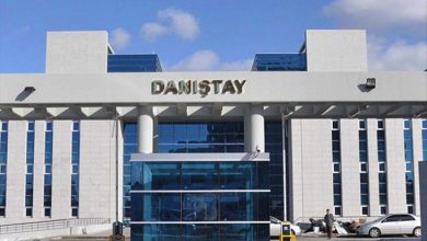 Modern mimariye sahip büyük bir kamu binasının giriş cephesi görülüyor. Üzerinde “Danıştay” yazısı yer alıyor. Cam kapılı ana girişin önünde birkaç kişi ve araç bulunuyor. Bina simetrik yapısıyla resmi ve kurumsal bir atmosfer yansıtıyor.