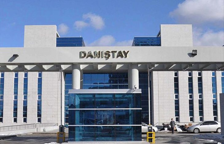 Modern mimariye sahip büyük bir kamu binasının giriş cephesi görülüyor. Üzerinde “Danıştay” yazısı yer alıyor. Cam kapılı ana girişin önünde birkaç kişi ve araç bulunuyor. Bina simetrik yapısıyla resmi ve kurumsal bir atmosfer yansıtıyor.