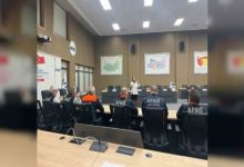 Bir toplantı salonunda AFAD personelleri oturmuş, ön tarafta ayakta duran bir kişi sunum yapıyor. Duvarlarda haritalar asılı; ortam resmi bir eğitim ya da bilgilendirme toplantısını andırıyor.