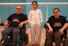 Aylin ve Ahmet Arslan çifti, spor salonunda tekerlekli sandalyede bulunuyor ve kızları ortada durarak poz veriyorlar.