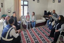 Mütevazı bir evin oturma odasında, birkaç kişi yarım daire şeklinde oturmuş sohbet ediyor. Ortada not tutan iki kadın dikkat çekiyor. Sağda başörtülü bir kadın elini uzatarak bir şeyi anlatıyor. Karşısında bir görevli ve diğer katılımcılar dikkatle dinliyor. Ortam, eğitim ya da bilgilendirme toplantısı havası veriyor.