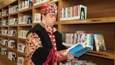Down sendromlu bir genç, bir kitaplıktan seçtiği kitabı dikkatle incelerken görülüyor. Üzerinde, Osmanlı dönemini simgeleyen, altın işlemeli kırmızı bir kaftan ve başında buna uyumlu, üzerinde mücevher detayı bulunan bir kavuk (başlık) bulunuyor.