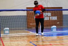 Kale önünde elinde top tutarak ayakta duran erkek goalball sporcusu kadraja yansıyor.