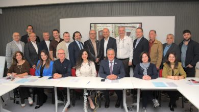 Geniş bir katılımcı grubunun bir toplantı salonunda, beyaz masaların etrafında ve arkasında toplu halde verdiği resmî bir heyet fotoğrafı. Katılımcılar profesyonel giyimli, ortam ise kurumsal bir toplantı atmosferini yansıtıyor.