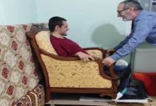 Ev ortamında bir sahne: Genç bir adam koltukta oturuyor, yanında duran orta yaşlı bir adam ise koltuğun altına eklediği düzenekle onu hareket ettirmeye hazırlanıyor. Görüntü, koltuğun tekerlekli sandalyeye dönüştürüldüğünü düşündürüyor; samimi ve emek dolu bir an.