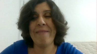 Mavi bluzlu, dalgalı kısa saçlı bir kadın, sade beyaz bir arka plan önünde gülümseyerek konuşuyor. Bir video görüşmesinden alınmış, yakın çekim bir kare.