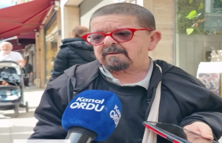 Sokakta yapılan bir röportajda, kırmızı çerçeveli gözlük takan bir adam mikrofonlara konuşuyor. Önünde “Kanal Ordu” yazılı bir mikrofon tutulurken, yanında bir telefon da kayıtta. Arka planda kafe ve yaya trafiği görülüyor; sahne gündelik bir sokak röportajını yansıtıyor.