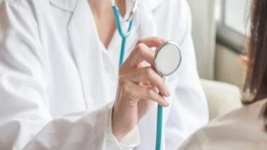 Beyaz önlüklü bir doktor, elinde stetoskopla bir hastayı muayene etmeye hazırlanıyor. Kadrajda doktorun üst kısmı ve hastanın omuz bölgesi görülüyor. Sahne, rutin bir sağlık kontrolü anını yansıtıyor.