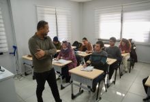 Bir sınıfta EKPSS hazırlık kursu alan öğrencileri ve başlarında duran bir eğitmeni gösteren fotoğraftır. Sınıftaki öğrenciler sıralarında ders çalışırken, eğitmen onlarla ilgilenmektedir. Odaklanmış ve eğitici bir atmosfer hakimdir.