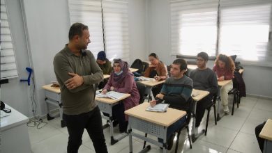 Bir sınıfta EKPSS hazırlık kursu alan öğrencileri ve başlarında duran bir eğitmeni gösteren fotoğraftır. Sınıftaki öğrenciler sıralarında ders çalışırken, eğitmen onlarla ilgilenmektedir. Odaklanmış ve eğitici bir atmosfer hakimdir.