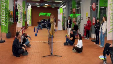 Görselde, bir spor etkinliği alanında oturarak voleybol oynayan kişiler görülüyor. Katılımcılar yerde oturur pozisyonda top alışverişi yaparken çevrede izleyenler ve destek olan kişiler bulunuyor. Etkinlik alanı Intercity logoları ve yeşil bayraklarla süslenmiş, enerjik ve hareketli bir atmosfer yansıtıyor.