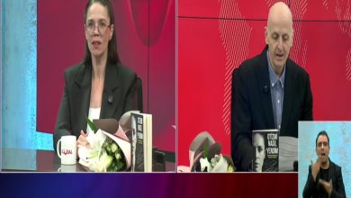 Bir televizyon programına ait ekran görüntüsü. Solda otizmli araştırmacı-yazar Espina Hande Ayas konuk, masada çiçek ve kitaplarla birlikte kameraya dönük konuşuyor. Sağda erkek sunucu Uğur Becerikli elindeki kitaptan okuyor. Alt köşede ise işaret dili tercümanı yer alıyor. Arka plan kırmızı tonlarda stüdyo dekoru.