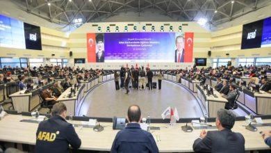 Geniş ve modern bir konferans salonunda, AFAD logosunun bulunduğu büyük ekranların önünde çok sayıda yetkili ve katılımcı, afet farkındalığına yönelik bir toplantı için yarım daire şeklinde oturma düzeninde bir araya gelmiş.