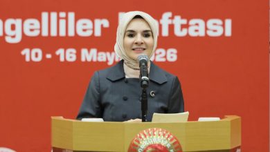Kürsüde konuşma yapan bir kadın, mikrofon önünde elindeki notlarla katılımcılara hitap ediyor. Arka plandaki kırmızı zeminde “Engelliler Haftası 10-16 Mayıs 2026” yazısı yer alırken, kürsüde Türkiye Büyük Millet Meclisi amblemi bulunuyor. Görsel, Engelliler Haftası kapsamında düzenlenen resmi bir panel konuşmasını yansıtıyor.